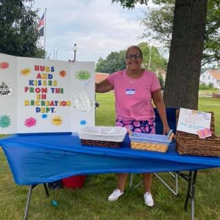 A woman stands behind a table with treats and a sign, "Hug and Kisses from the EH Recreation Dept